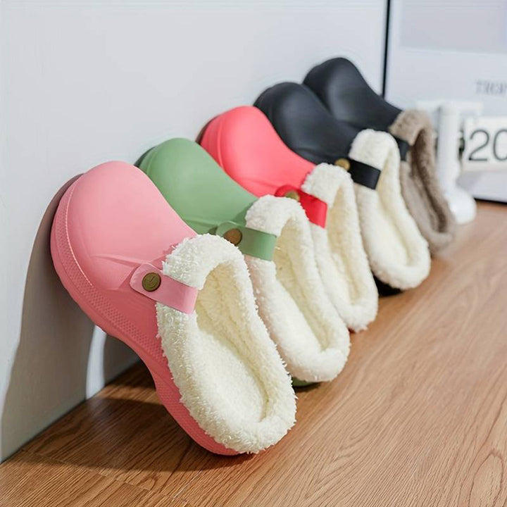 Vijf paar kleurrijke, warme klompen met bontvoering op houten vloer. Comfortabele winterpantoffels in roze, groen, zwart en meer.