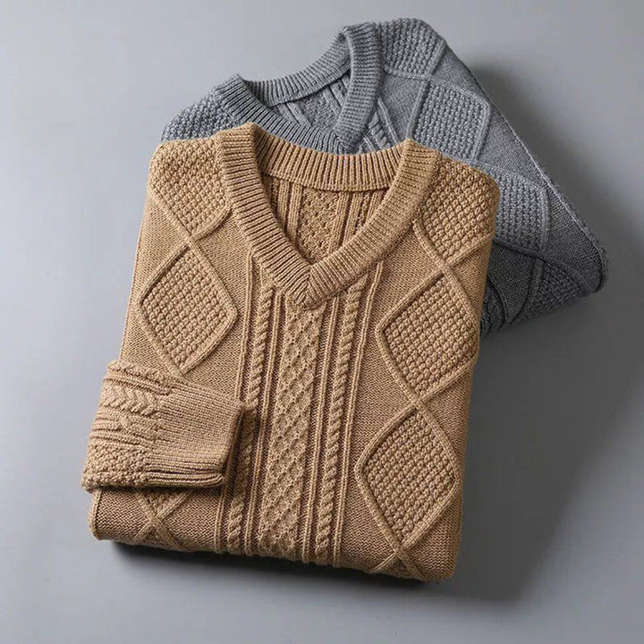 Twee gebreide truien, beige en grijs, met V-hals en kabelpatroon, opgevouwen op een grijze achtergrond. Perfect voor herfst- en wintermode.