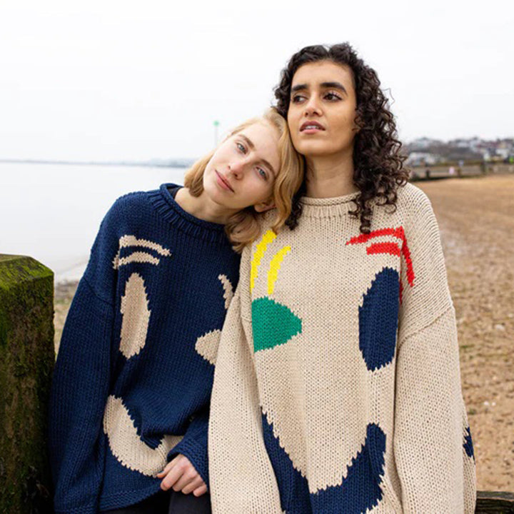 Twee vrouwen dragen kleurrijke truien met lachende gezichten op een strand. Mode, herfstkleding, gebreide truien, casual stijl, strandwandeling.