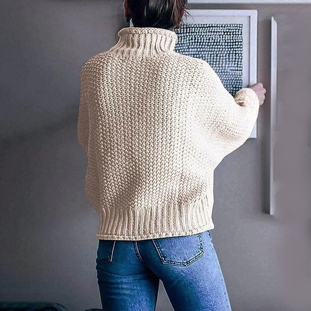 Vrouw in gebreide crèmekleurige trui met hoge kraag, casual stijl, rugaanzicht, gecombineerd met blauwe jeans, moderne interieurdecoratie.