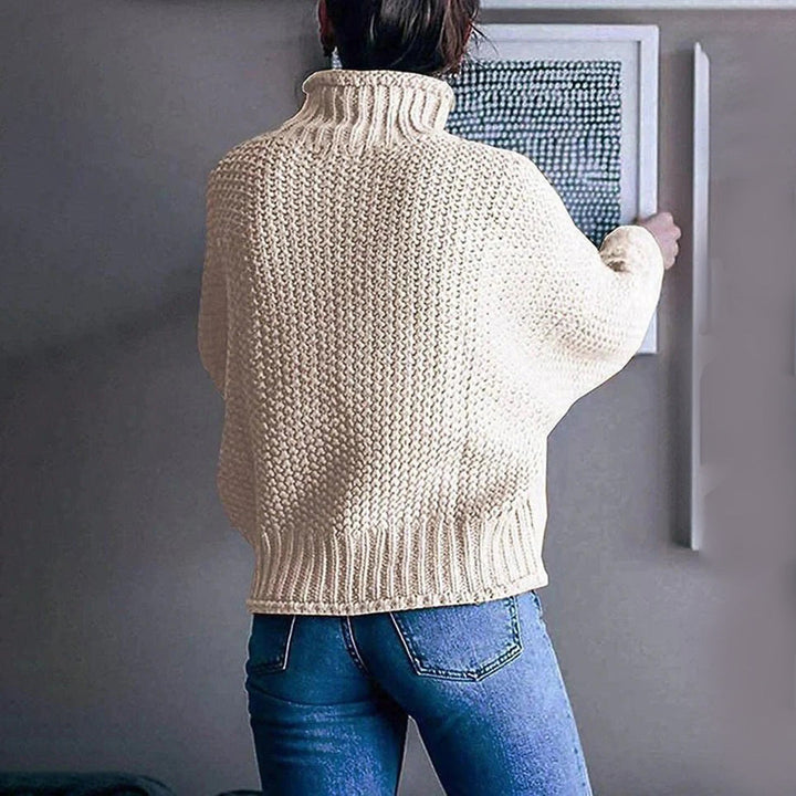 Vrouw in gebreide crèmekleurige trui met hoge kraag, casual stijl, rugaanzicht, gecombineerd met blauwe jeans, moderne interieurdecoratie.