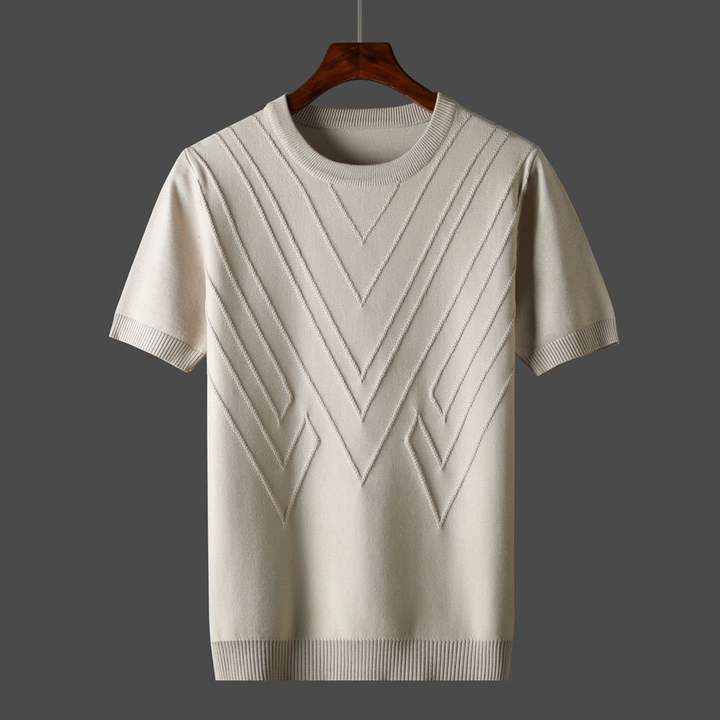 Crèmekleurige gebreide trui met korte mouwen en geometrisch patroon, hangend aan houten hanger. Perfect voor casual en stijlvolle outfits.