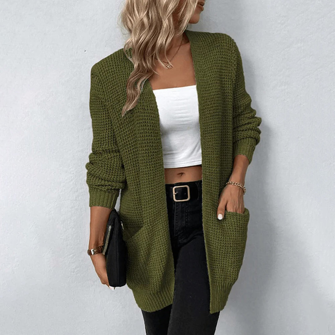 Vrouw draagt een olijfgroene gebreide cardigan met zakken, gecombineerd met een witte top en zwarte broek. Stijlvolle herfstmode, casual outfit.