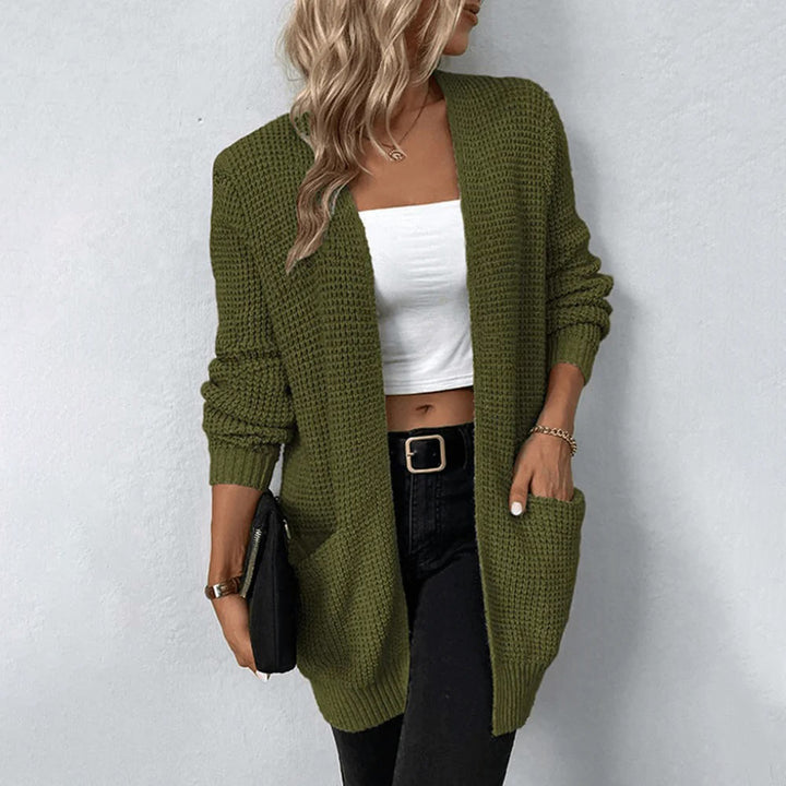 Vrouw draagt een olijfgroene gebreide cardigan met zakken, gecombineerd met een witte top en zwarte broek. Stijlvolle herfstmode, casual outfit.