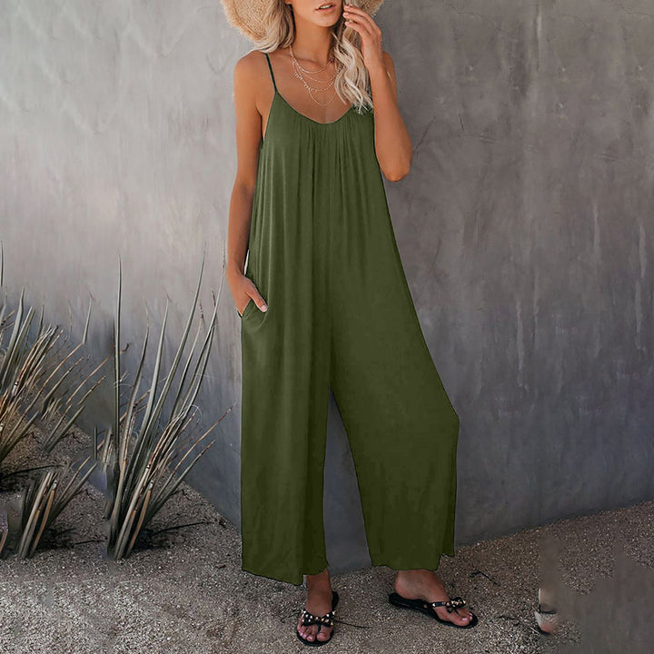 Vrouw in een casual legergroene jumpsuit met spaghetti bandjes, staand tegen een grijze muur. Zomerse outfit, trendy mode, comfortabele stijl.