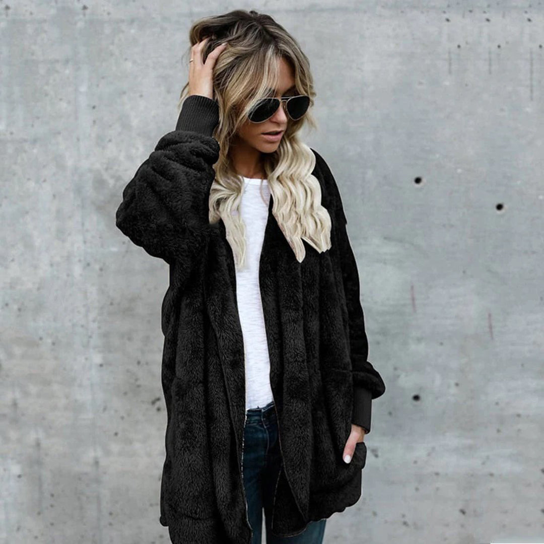 Vrouw in zwarte faux fur jas, witte trui en zonnebril tegen betonnen muur. Modieuze winterkleding, casual stijl, trendy damesmode.