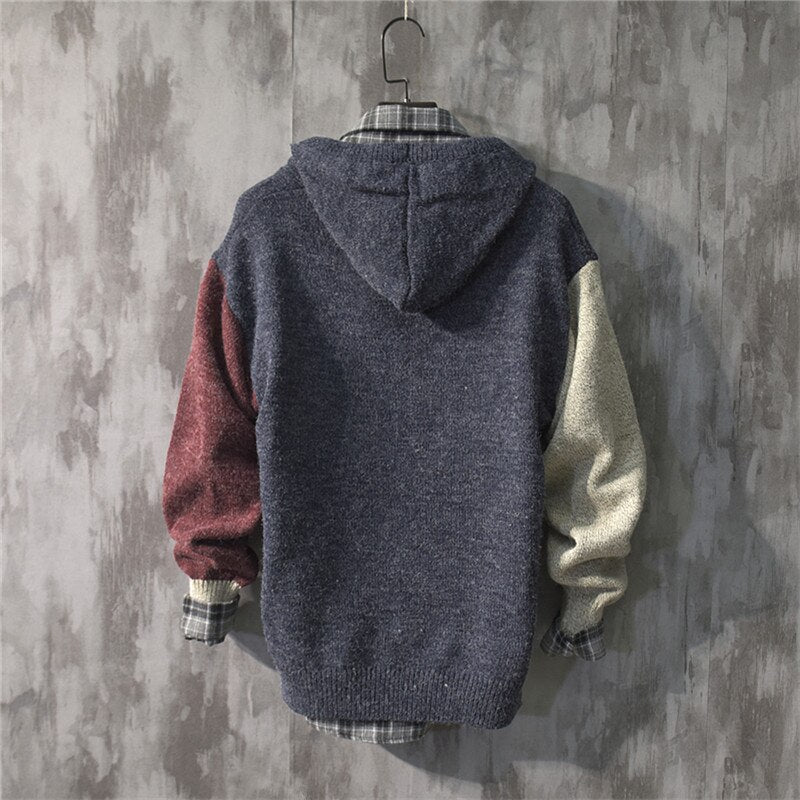 Grijze hoodie met contrasterende mouwen in rood en beige, opgehangen aan een haak tegen een betonnen muur. Modieuze herenkleding, casual stijl.