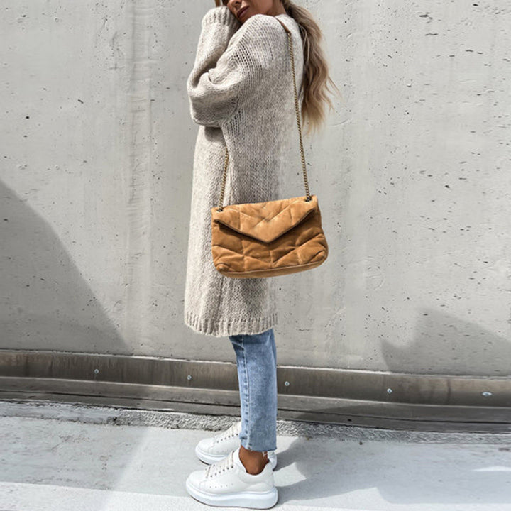 Vrouw in beige gebreide trui, blauwe jeans en witte sneakers met bruine schoudertas. Modieuze herfstoutfit, casual streetwear stijl.