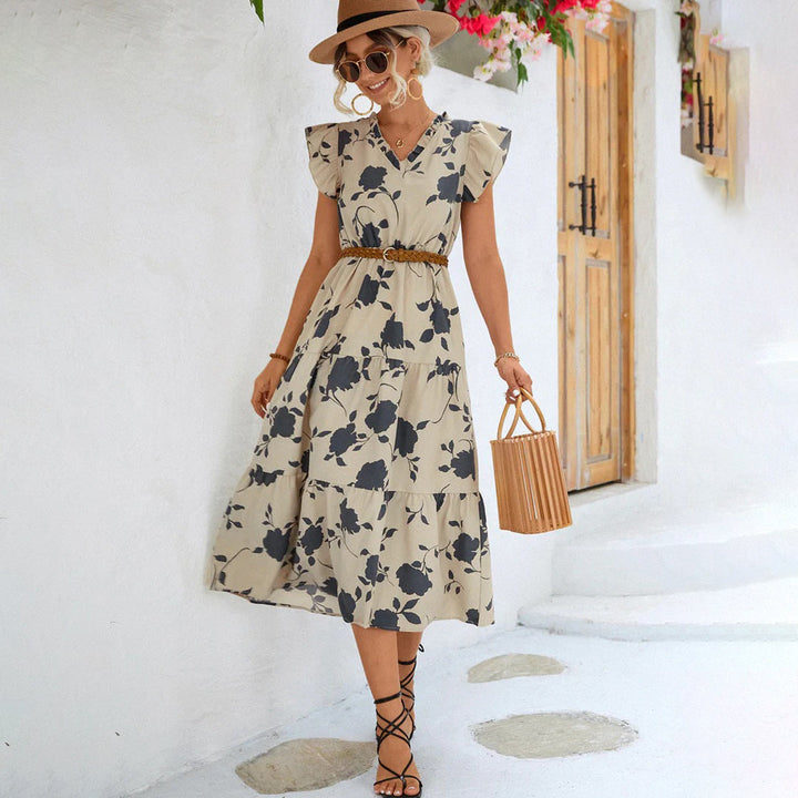 Vrouw in beige zomerjurk met bloemenprint, strohoed en houten handtas, poseert voor witte muur. Zomermode, casual dameskleding, boho stijl.