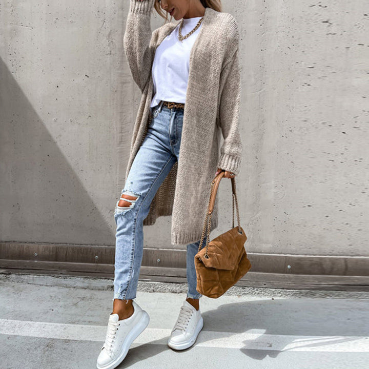Vrouw in casual outfit met beige gebreid vest, witte sneakers, gescheurde jeans en bruine tas. Modieuze herfstkleding, streetwear stijl.