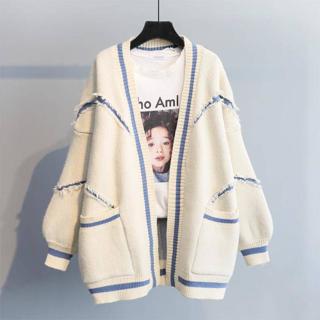 Beige oversized cardigan met blauwe strepen en gerafelde details, hangend aan een hanger. Perfect voor casual mode en herfstoutfits.