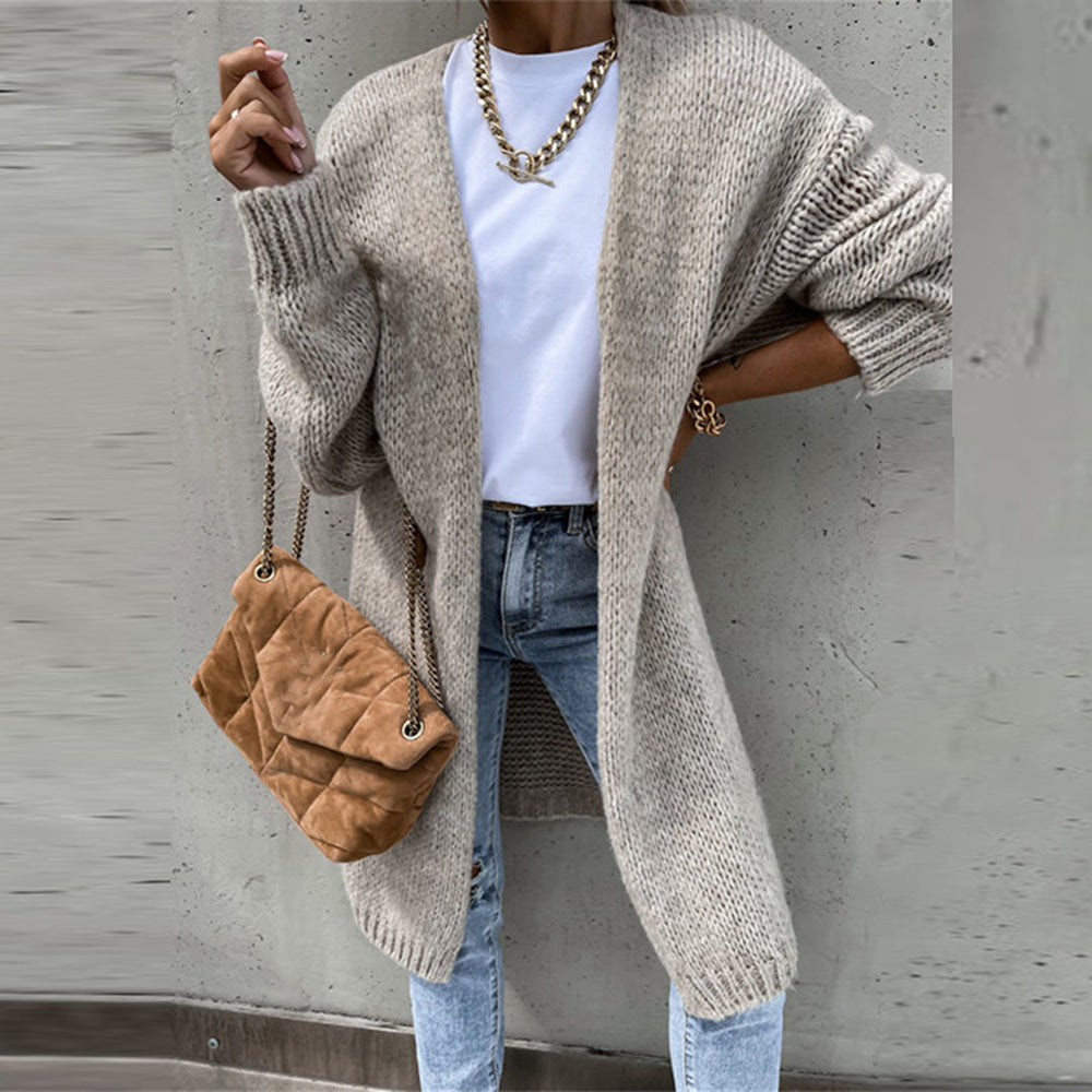 Vrouw in beige gebreid vest, witte top en blauwe jeans, draagt een bruine schoudertas. Modieuze herfstoutfit, casual dameskleding.