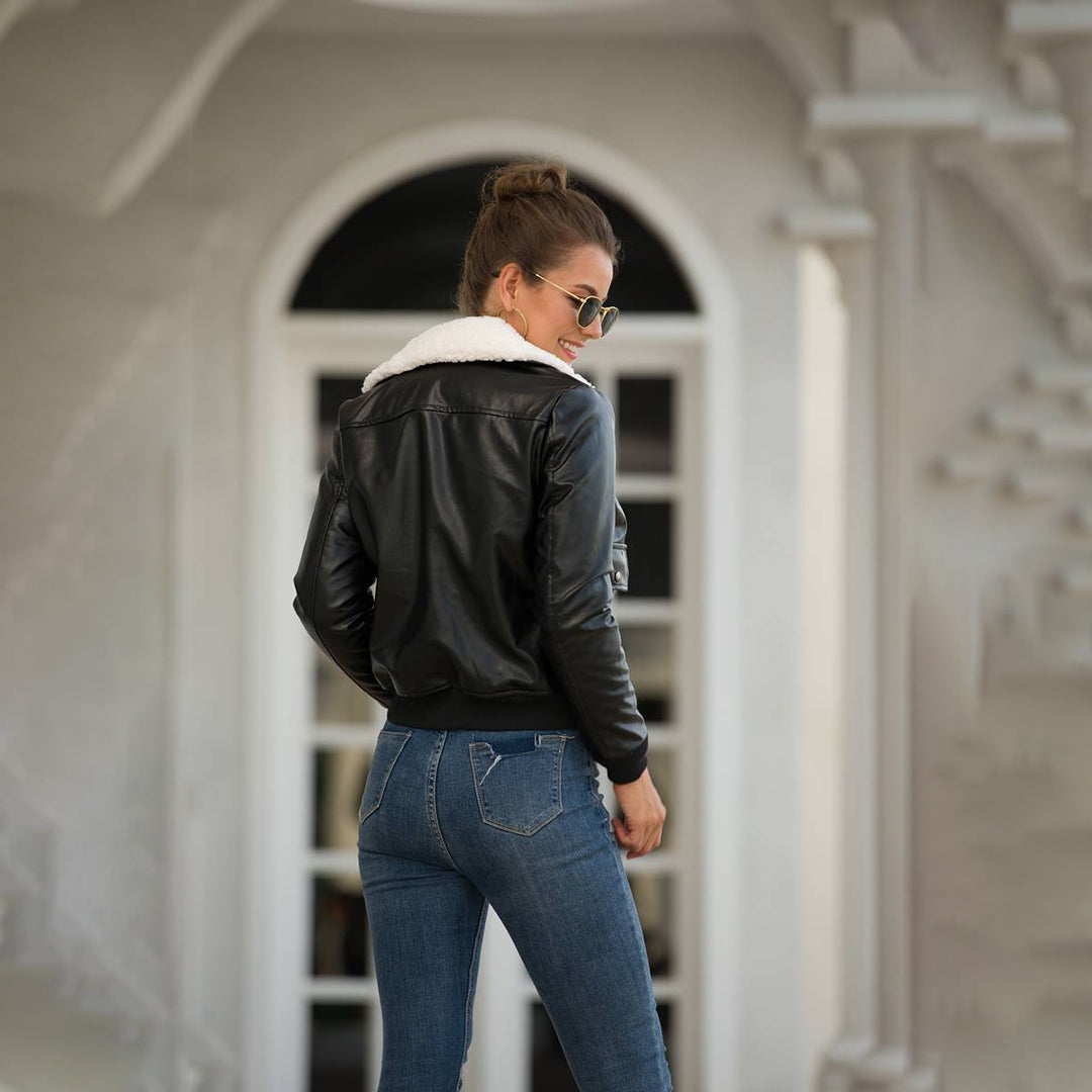 Vrouw in zwarte leren jas met witte kraag, blauwe jeans, zonnebril, staand voor een klassieke witte deur. Modieuze dameskleding, herfststijl.