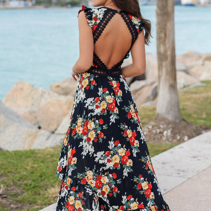 Vrouw in elegante zwarte bloemenjurk met open rug, staand bij water en bomen. Zomerse mode, stijlvolle jurk, bloemenprint, open rugontwerp.