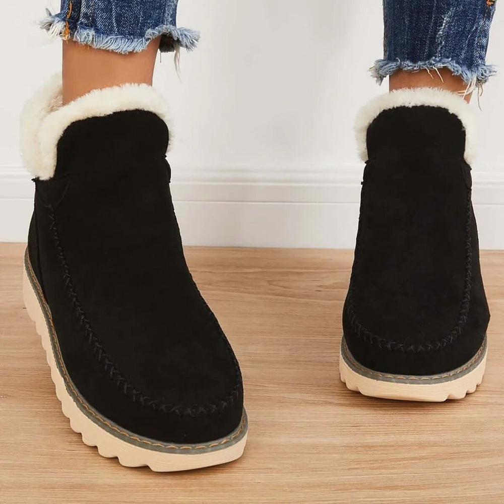 Zwarte suède enkellaarsjes met witte voering, dikke rubberen zool en stikseldetails, perfect voor wintermode en casual outfits.