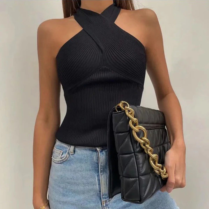 Vrouw in zwarte, mouwloze top met gekruiste halslijn, draagt een zwarte gewatteerde tas met gouden ketting, casual jeans. Modieuze dameskleding.