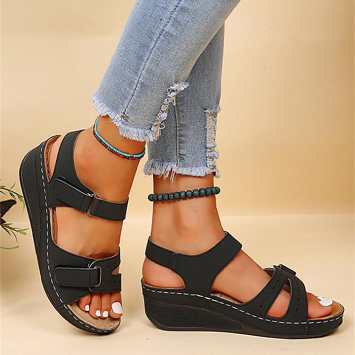 Zwarte dames sandalen met sleehak, verstelbare riemen en comfortabele zool, gedragen met gescheurde jeans. Perfect voor zomerse casual outfits.