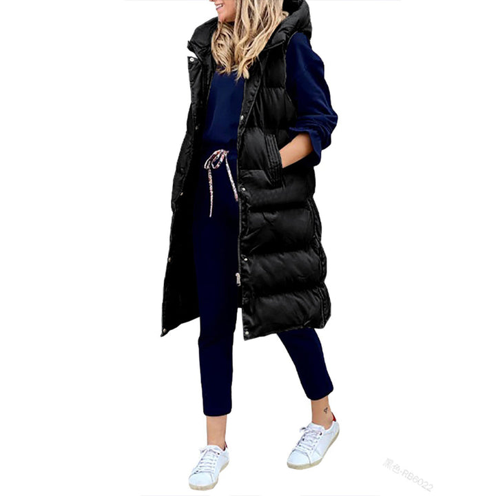 Vrouw in lange zwarte gewatteerde bodywarmer met capuchon, blauwe joggingbroek en witte sneakers. Modieuze winterkleding, casual stijl.