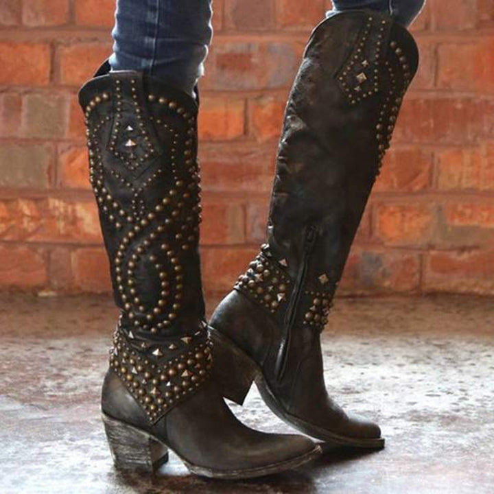 Zwarte leren cowboylaarzen met studs, hoge hak en ritssluiting, gedragen voor een bakstenen muur. Perfect voor damesmode en westerse stijl.