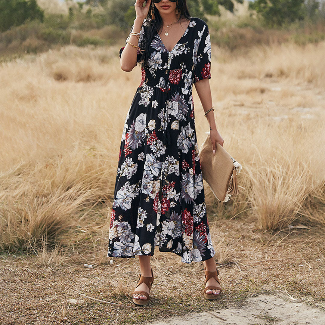 Vrouw in zwarte bloemenjurk met korte mouwen, staand in een veld. Zomerjurk, casual mode, bohemian stijl, elegante dameskleding.
