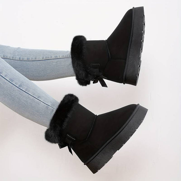 Zwarte dameslaarzen met bontvoering, platte zool en strikdetail, gedragen met lichtblauwe jeans. Wintermode, comfortabele warme schoenen.