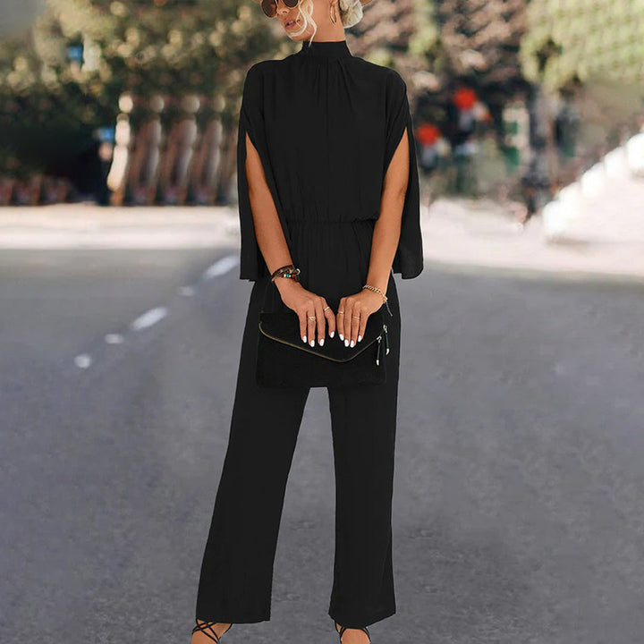 Vrouw in elegante zwarte jumpsuit met wijde pijpen en hoge hals, draagt zonnebril en zwarte clutch, modieuze straatstijl.