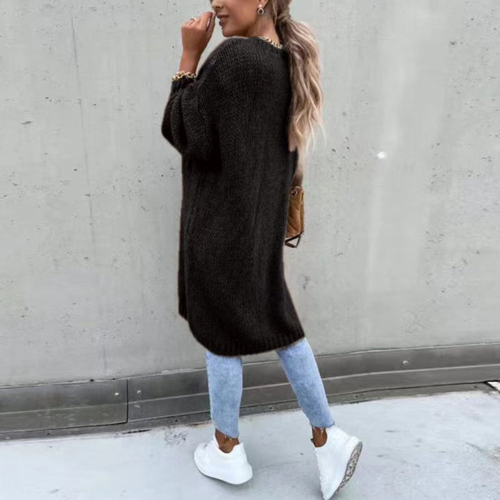 Vrouw in zwarte oversized trui, blauwe jeans en witte sneakers, poseert tegen een grijze muur. Modieuze herfstoutfit, casual streetwear stijl.