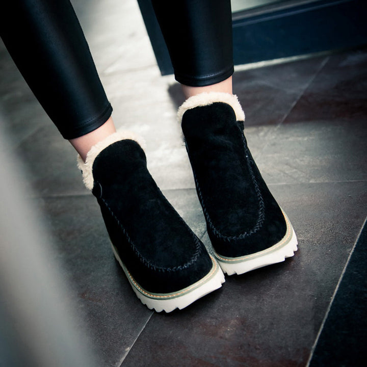 Zwarte suède enkellaarsjes met witte zool en warme voering, gedragen door model. Trendy wintermode, comfortabele dameslaarzen, casual stijl.