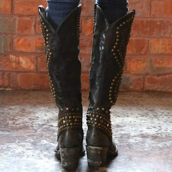 Zwarte leren cowboylaarzen met studs, gedragen door persoon tegen bakstenen muur. Trendy westernstijl, damesmode, robuuste laarzen.