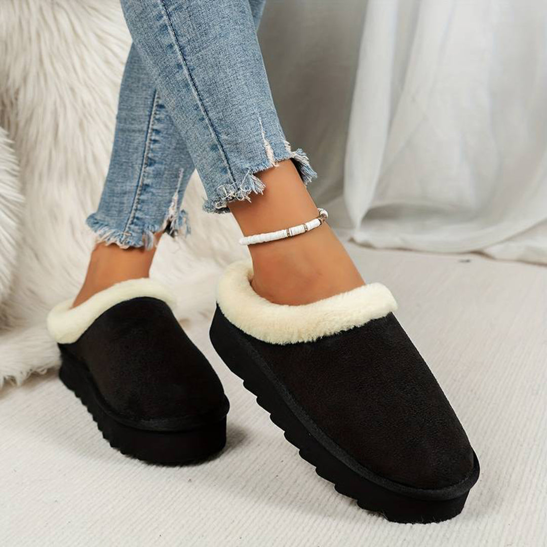 Zwarte dames pantoffels met witte voering, gedragen met gescheurde jeans. Comfortabele winterse huisschoenen, ideaal voor warme voeten thuis.