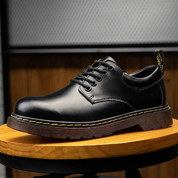 Zwarte leren herenschoen met veters, stevige bruine zool en gele stiksels, ideaal voor casual en formele gelegenheden. Stijlvolle en duurzame schoenen.