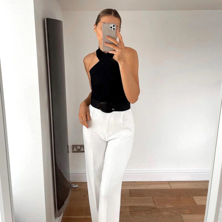 Vrouw in zwarte haltertop en witte broek maakt selfie in moderne kamer. Stijlvolle mode, minimalistisch interieur, trendy outfit.