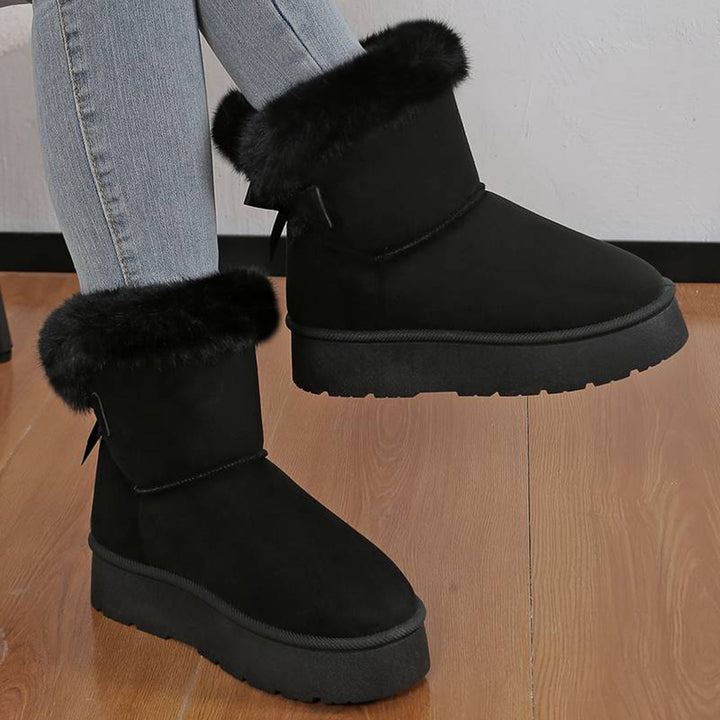 Zwarte winterlaarzen met bontvoering, gedragen door persoon in spijkerbroek, op houten vloer. Warme dameslaarzen, trendy en comfortabel.