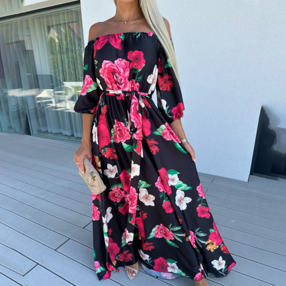 Vrouw in zwarte off-shoulder jurk met rode en witte bloemenprint, staand op terras. Elegante zomerjurk, modetrend, casual chique stijl.