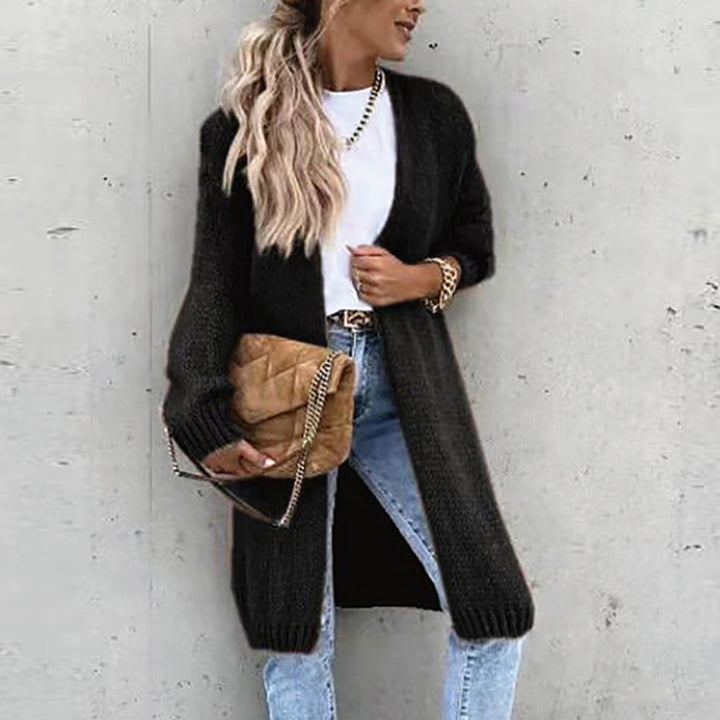 Vrouw in zwarte gebreide cardigan, witte top en blauwe jeans, met een bruine gewatteerde schoudertas. Modieuze herfstoutfit, casual stijl.