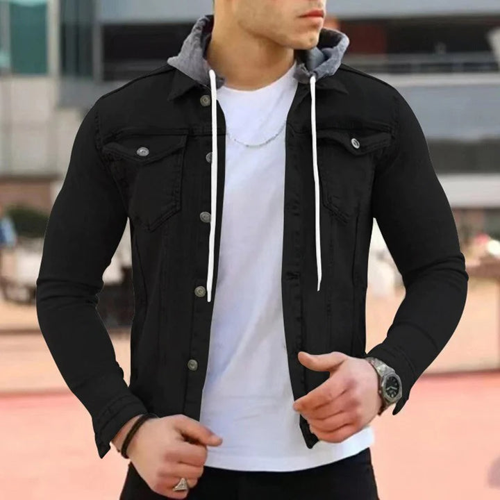 Man in zwarte spijkerjas met grijze capuchon, witte T-shirt, zilveren ketting en horloge. Stijlvolle herenkleding, casual mode.