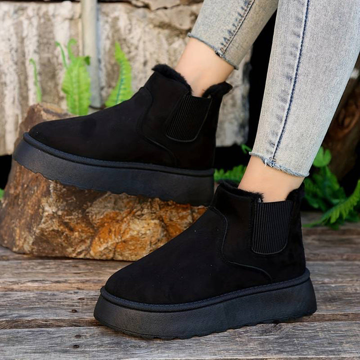 Zwarte suède enkellaarsjes met dikke zool, elastische inzet en bontvoering, gedragen met lichtblauwe jeans. Perfect voor wintermode en comfort.