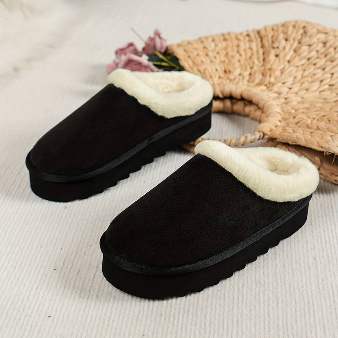 Zwarte pluche pantoffels met witte voering op een beige achtergrond, perfect voor wintercomfort en warmte. Ideaal voor thuisgebruik.