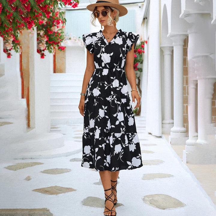 Vrouw in zwart-witte bloemenjurk met hoed, wandelend in mediterrane straat. Zomermode, elegante jurk, casual stijl, vakantie outfit.