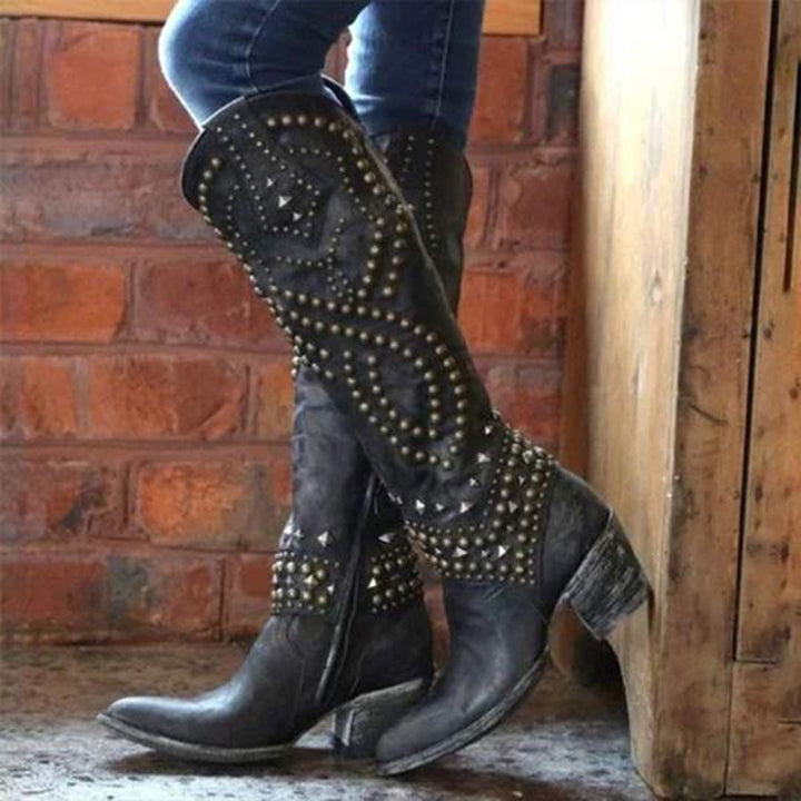 Zwarte leren laarzen met studs, gedragen door persoon tegen bakstenen muur. Trendy damesmode, stoere westernstijl, hoge laarzen.