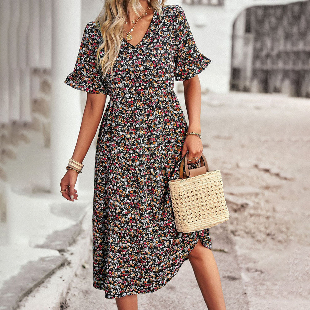 Vrouw in zwarte bloemenjurk met korte mouwen en rieten tas, zomermode, casual outfit, buiten gefotografeerd.