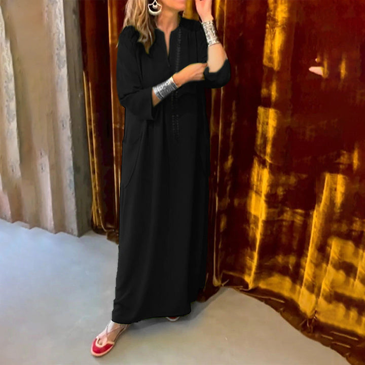 Zwarte kaftan jurk met lange mouwen, gedragen door vrouw met zilveren armbanden, voor een fluwelen achtergrond. Elegante damesmode, avondkleding.