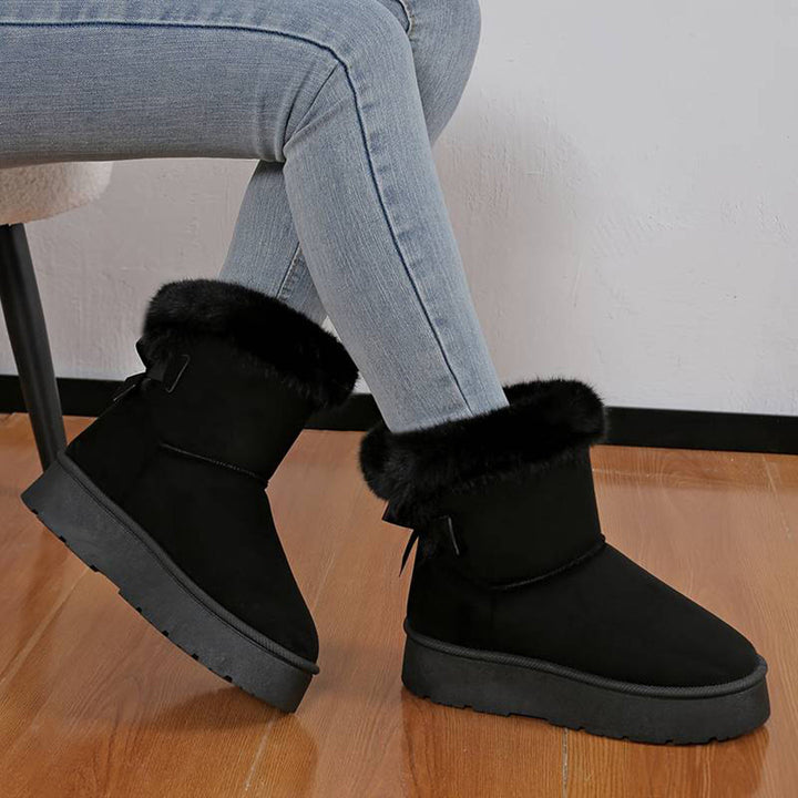 Zwarte dameslaarzen met bontvoering, gedragen met blauwe jeans. Warme winterlaarzen, comfortabele schoenen, casual stijl, houten vloer.