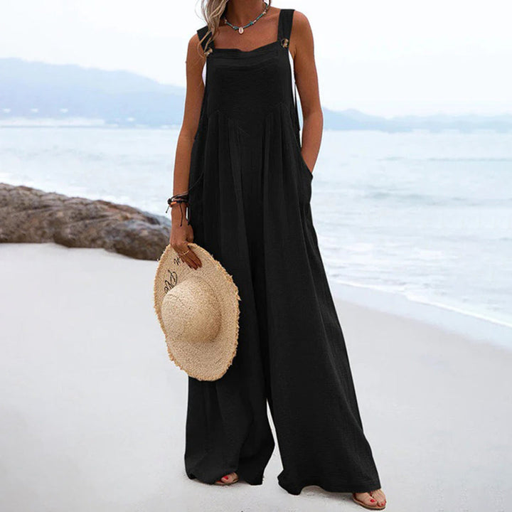 Vrouw in zwarte zomerjurk op strand, met strohoed in hand. Casual strandmode, comfortabele wijde pasvorm, ideaal voor zomerse dagen.