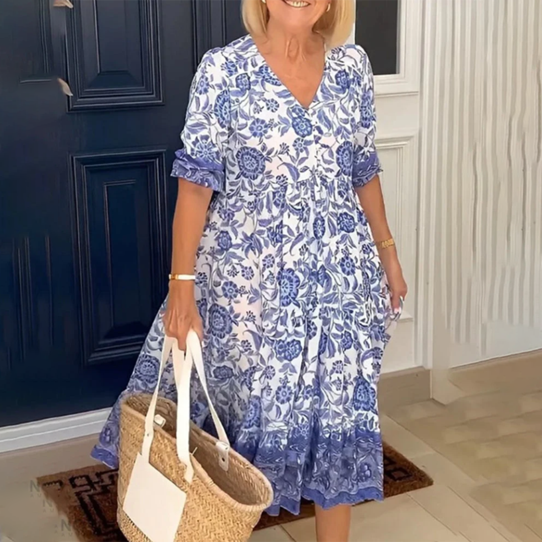 Vrouw in blauwe bloemenjurk met rieten tas voor donkerblauwe deur. Zomermode, casual dameskleding, elegante outfit.