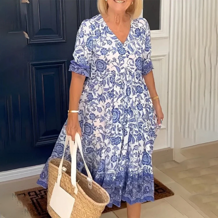 Vrouw in blauwe bloemenjurk met rieten tas voor donkerblauwe deur. Zomermode, casual dameskleding, elegante outfit.