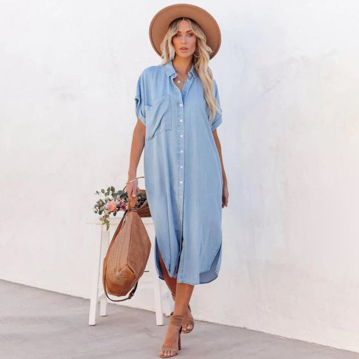 Vrouw in lichtblauwe maxi-jurk met knopen, draagt een bruine hoed en sandalen, houdt een grote bruine tas vast. Zomerse mode, casual stijl.