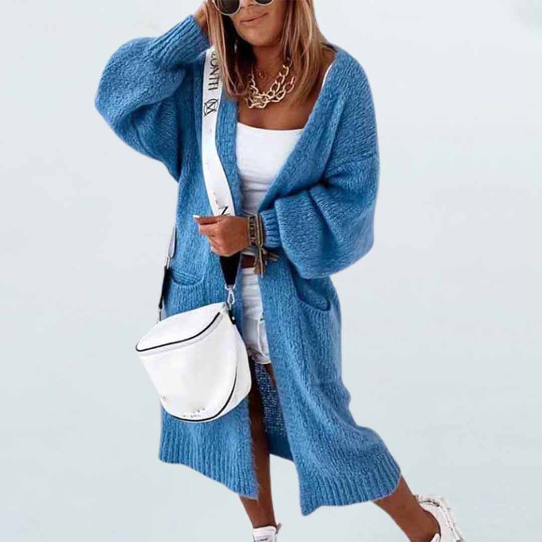Blauwe gebreide damescardigan met lange mouwen, gecombineerd met witte tas en sneakers. Modieuze herfstoutfit voor casual stijl.