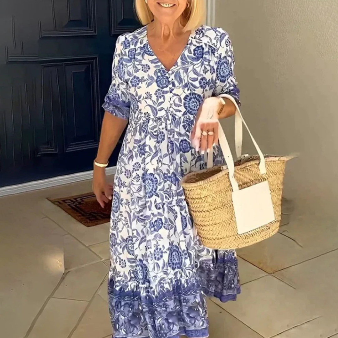 Vrouw in blauwe bloemenjurk met rieten tas, staand voor een donkerblauwe deur. Zomerse mode, casual stijl, elegante dameskleding.