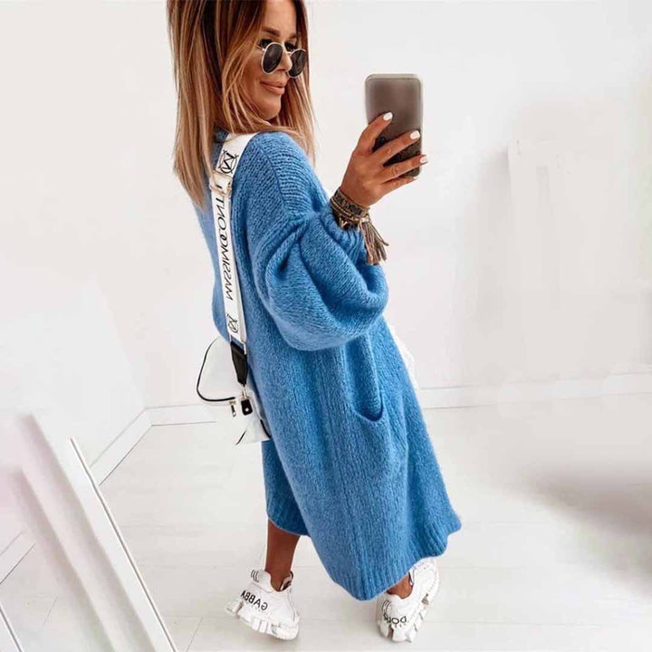 Vrouw in blauwe oversized trui met lange mouwen, witte sneakers en zonnebril, maakt selfie. Modieuze dameskleding, casual stijl.